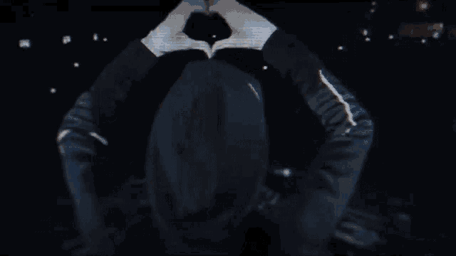 a person making a heart shape with their hands in a dark room