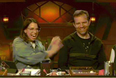 a man and a woman are sitting at a table with their hands in the air and laughing .