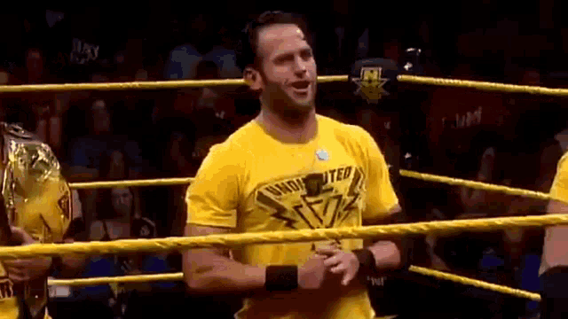 a man wearing a yellow shirt is standing in a wrestling ring .