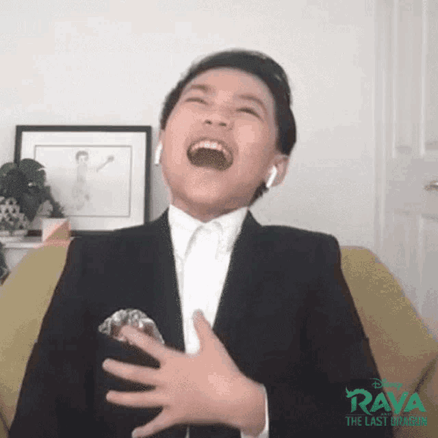 a young boy in a suit and tie is laughing while wearing ear buds .