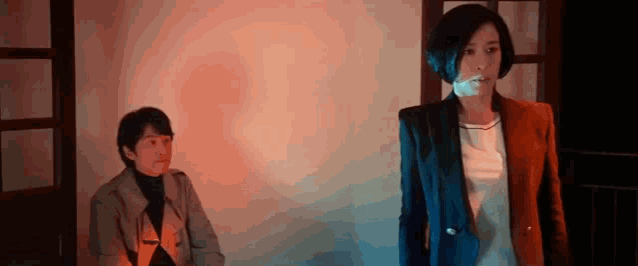 a man and a woman are standing next to each other in a dark room . the woman is smoking a cigarette .
