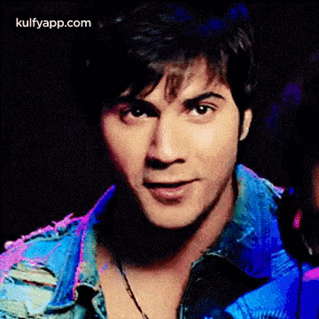 a close up of a man 's face wearing a blue denim jacket and a necklace .