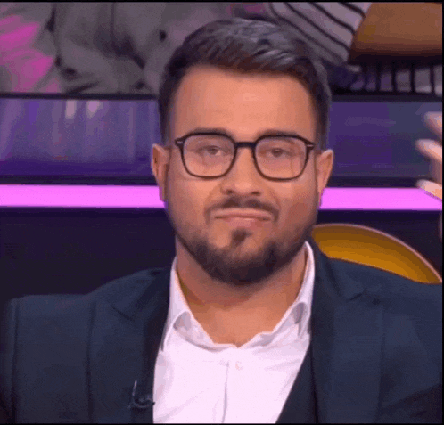a man with a beard wearing glasses and a suit is making a face .