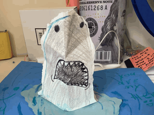 a child 's drawing of a shark is on a table next to a can of federal reserve note