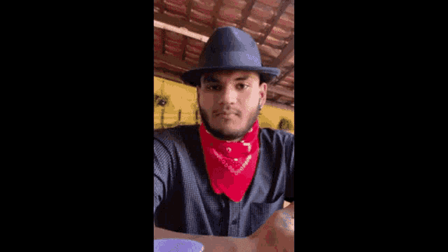 a man wearing a fedora hat and a red bandana is giving a peace sign