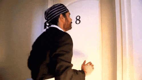 a man wearing a striped hat stands in front of a door with the number 8 on it
