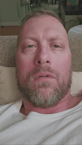 a man with a beard and green eyes is laying on a couch with his eyes closed