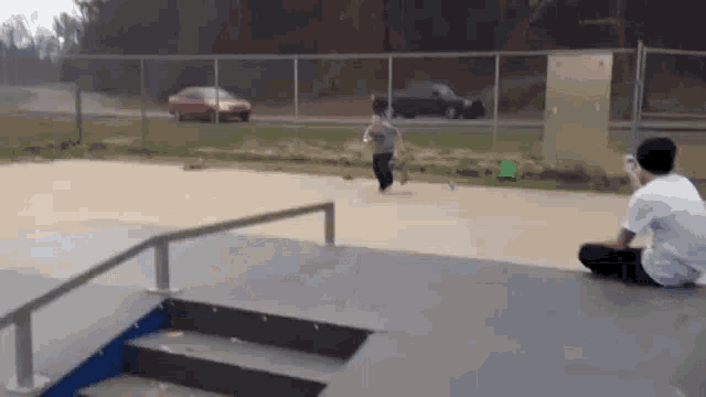 a man is sitting on a ramp at a skate park while a boy runs down the ramp .