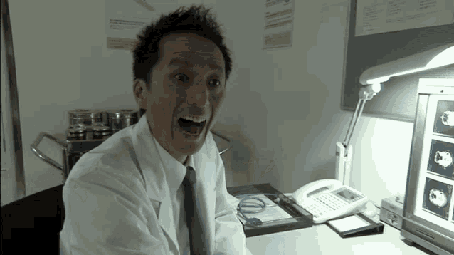 a man in a lab coat is sitting at a desk with his mouth wide open