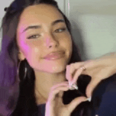 a woman is making a heart shape with her hands and smiling .