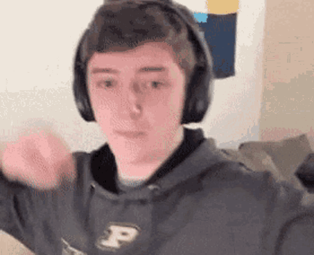 a young man wearing headphones and a hoodie with the letter p on it is making a funny face .