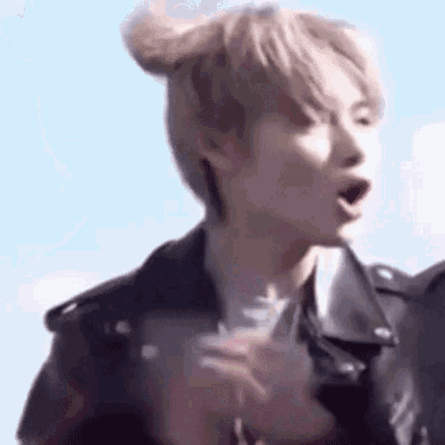 a close up of a person wearing a leather jacket and a bun with their mouth open .