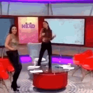 two women are dancing in a room with a sign that says nexo on it .