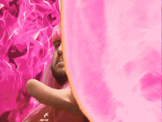 a man with pink hair and a beard is holding a pink cloth in front of a pink background .