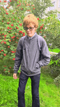 a young boy wearing glasses and a backpack stands in front of a tree with red berries