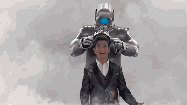 a boy wearing a crown stands in front of a silver robot