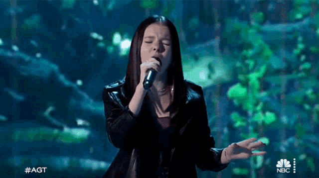 a young woman is singing into a microphone on a stage in front of a green background .
