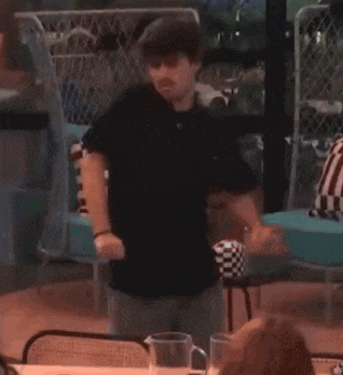 a man in a black shirt is swinging a bat at a table