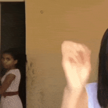 a girl in a white dress is standing in front of a door while another girl stands behind her .