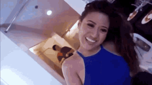 a woman in a blue tank top is smiling in a room with a man standing in the background .