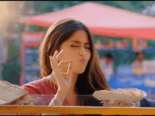 a woman is making a funny face while eating a hot dog at a food stand .