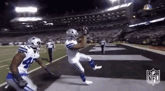 a football player is catching a pass on a field while another player watches .