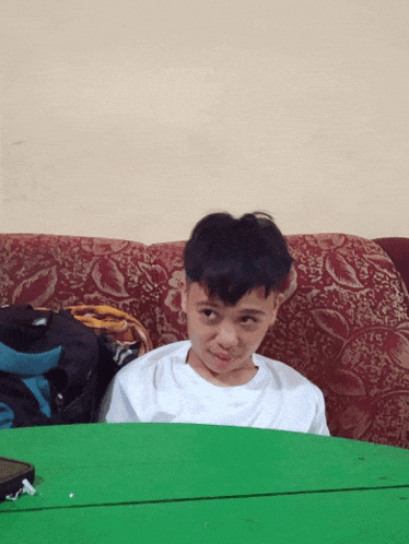 a young boy sitting on a couch with a green table behind him