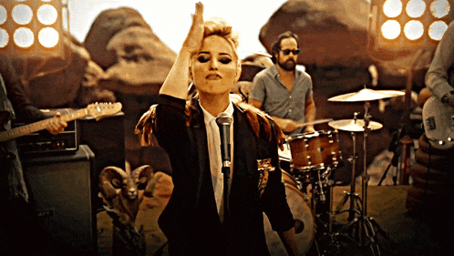 a woman singing into a microphone with a man playing drums behind her