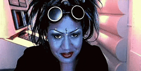 a woman with blue paint on her face and goggles on her head looks at the camera .
