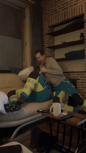 two men are sitting on a couch laughing and one is wearing a safety vest