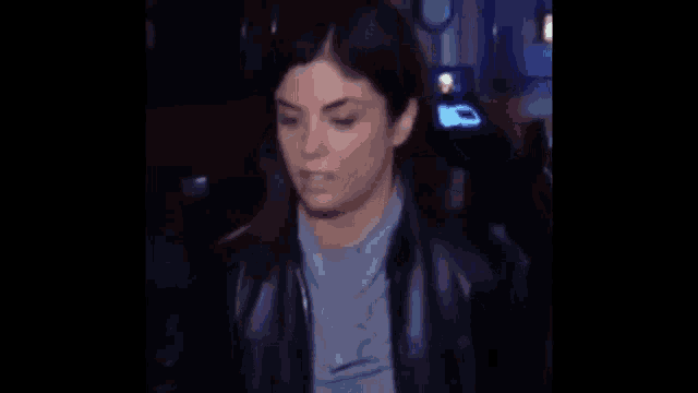 a woman is standing in a dark room wearing a black leather jacket .