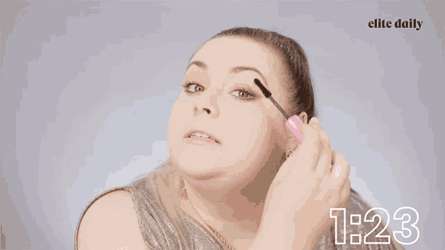 a woman is applying mascara in front of a banner that says yasssss