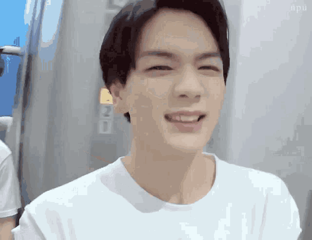 a young man wearing a white t-shirt is smiling .