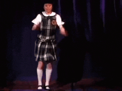 a girl in a plaid dress is standing on a stage with a purple curtain behind her