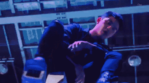 a man in a blue jacket is covering his face with his hand in a dark room .