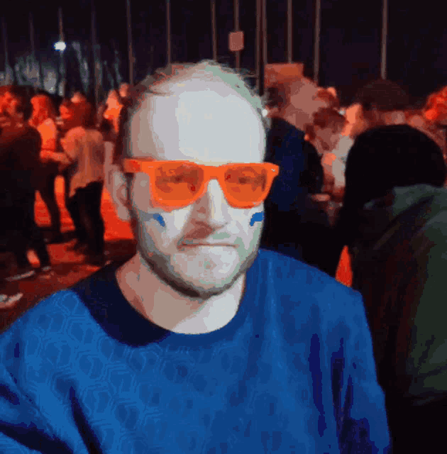a man wearing orange sunglasses and a blue shirt is standing in a crowd