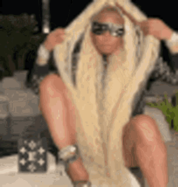 a woman with long blonde hair is sitting on the ground with a scarf around her head .
