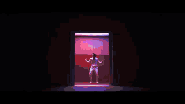 a man in a white suit is dancing in front of a pink wall .