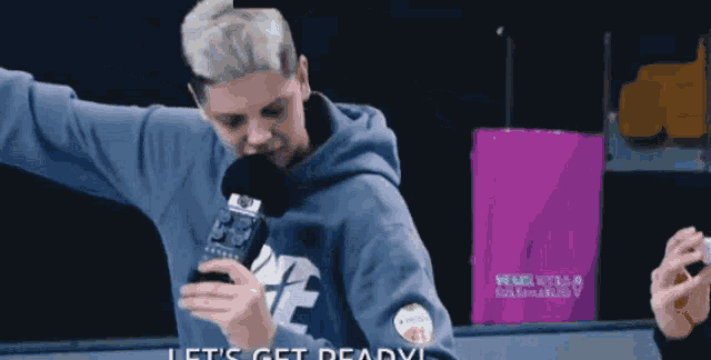 a man in a blue hoodie holds a microphone and says let 's get dead