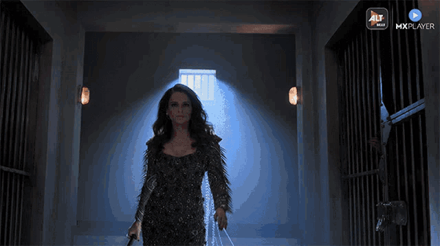a woman in a black dress is walking down a dark hallway with a mxplayer logo on the bottom