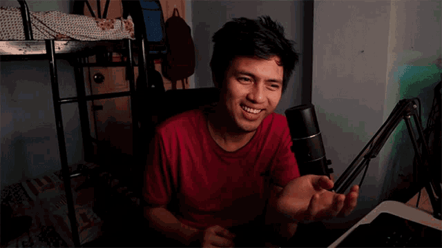 a man in a red shirt is sitting in front of a microphone and smiling