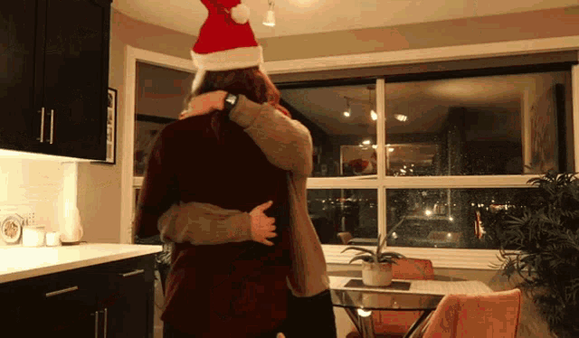 a woman wearing a santa hat is hugging a man