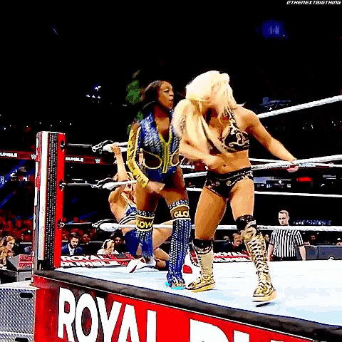 two women are wrestling in a wrestling ring with a royal rumble sign in the background .