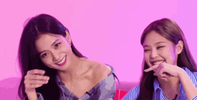 two women are sitting next to each other on a pink background .