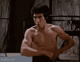 bruce lee is flexing his muscles in a boxing ring without a shirt on .