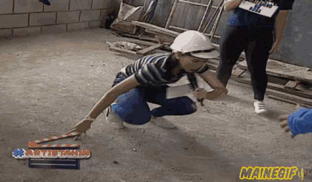 a woman wearing a hard hat is kneeling on the ground in front of a mainegif sign