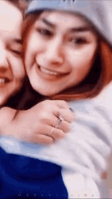 two women are hugging each other and smiling for the camera . one of the women is wearing a ring on her finger .