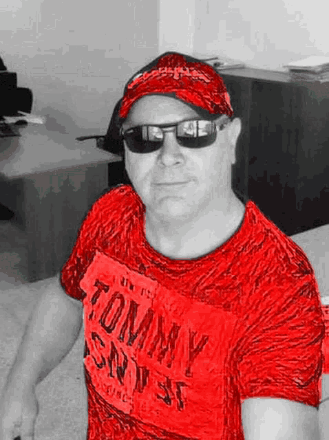 a man wearing a red shirt , sunglasses and a red hat is sitting in an office .
