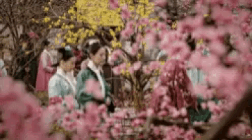 a group of people are standing in a garden surrounded by pink flowers .