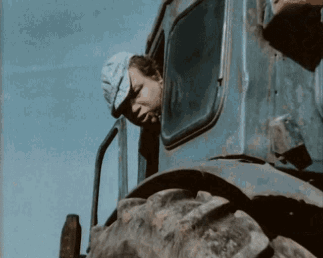 a man in a hat looks out of the window of a blue vehicle